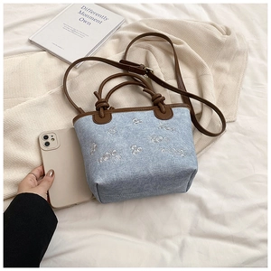 Close-up of mini denim bucket bag with floral embroidery and brown leather trim detailing