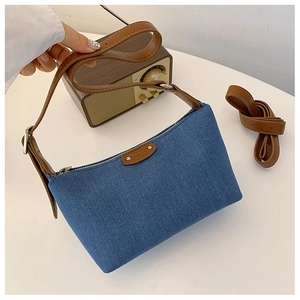 Detail of blue denim baguette bag with brown leather trim and silver metal hardware