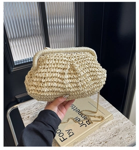 Detail of beige straw shell bag with woven texture and gold chain strap held by hand