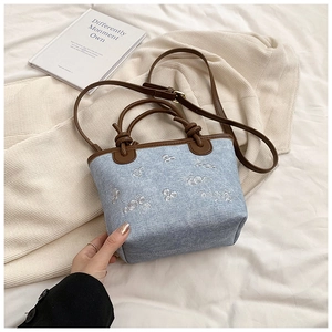 Close-up of light blue denim bucket bag with white floral embroidery and brown handles