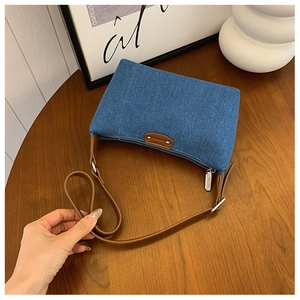 Detail of vintage blue denim hobo bag with brown leather strap on a wooden table