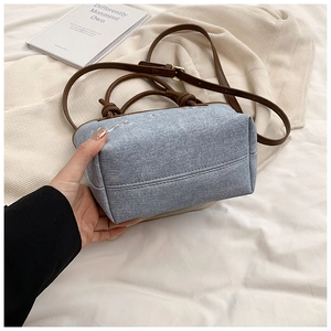 Detail of light blue denim bucket bag with brown leather handles and sturdy base