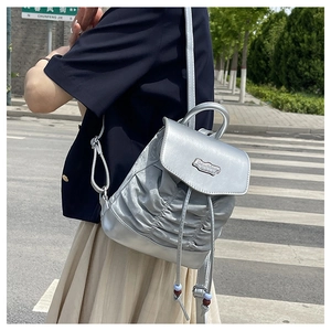 Outdoor shot of a silver metallic pleated mini backpack with a stylish flap and top handle