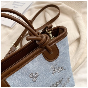 Detailed view of floral embroidery on light blue denim bag with brown leather handles