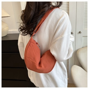 Detail of vibrant orange nylon crescent bag with wide shoulder strap on white sweater