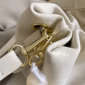 Macro detail of high-quality gold hardware hook on pearl white textured bucket bag
