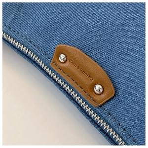 Detail of blue denim fabric with silver zipper and engraved brown leather brand patch