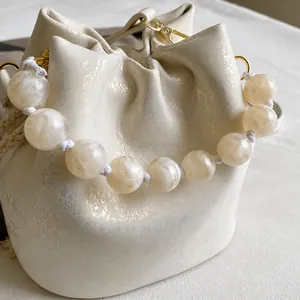 Detail of off-white bucket bag featuring large marble-texture pearl handle and gold hardware