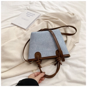 Detail of denim bucket bag showing knotted brown leather handles and adjustable strap