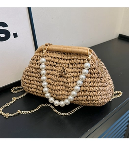 Close-up of woven straw cloud bag featuring white pearl handle and gold chain strap