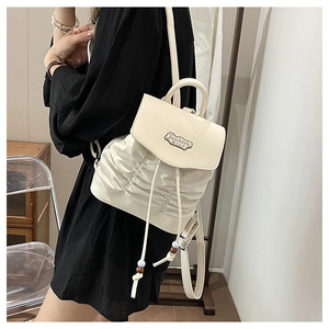 Detail of cream white pleated backpack featuring decorative drawstring beads and metal tag