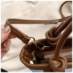 Detail of brown leather handbag handle with knot design and gold metal hardware hook