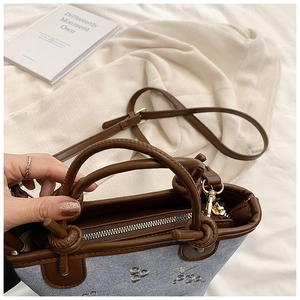 Detail of light blue denim bucket bag featuring sequins, brown handles and gold zipper