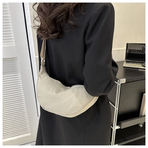 Beige crescent crossbody bag shown worn by a model in a minimalist home setting
