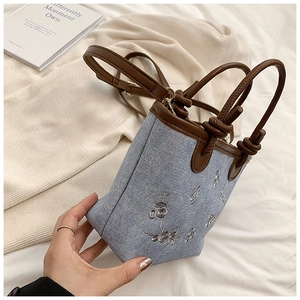 Detail of floral embroidery on light blue denim bucket bag with brown leather handles