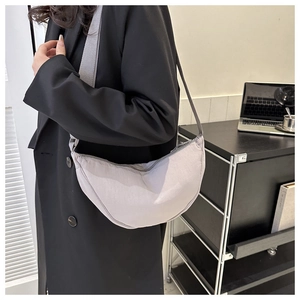 Detail of light purple pleated crescent bag with wide nylon strap on model in black suit