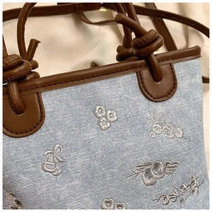 Detailed close-up of floral embroidery on blue denim and brown leather knotted handle