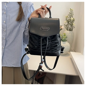 Detail of black pleated leather backpack featuring a metal Fashion logo and bead drawstring
