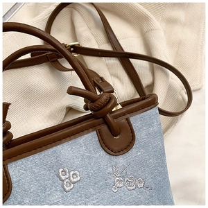 Detail of light blue denim bucket bag with brown leather trim and floral embroidery