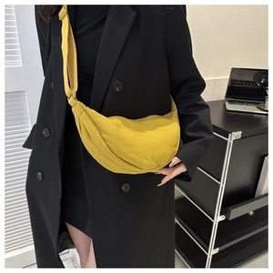 On-body shot of a bright yellow dumpling crossbody bag with adjustable strap over a black suit