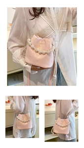 Macro view of a pink pleated bucket bag featuring elegant pearl handles and drawstring detail