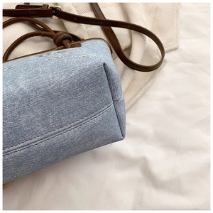 Detail of light blue denim bucket bag with brown leather knotted handle and golden buckle