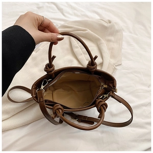 Detail of brown faux leather bucket bag with knot handle and gold zipper interior