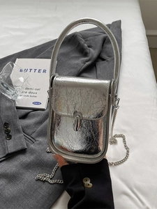 Silver metallic crossbody bag with chain strap on grey blazer and white bedding