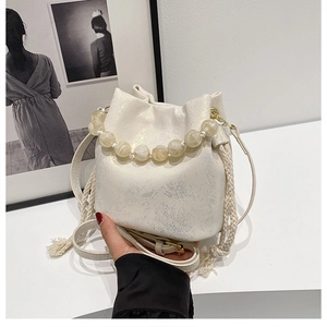 Detail of cream pleated bucket bag featuring marble beaded handle and braided rope accents