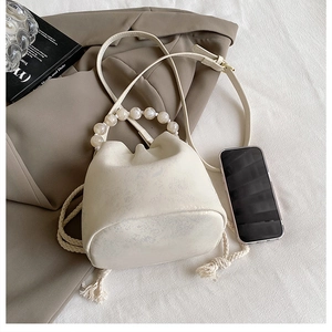 Detailed top view of cream drawstring bucket bag with beaded handle and leather strap