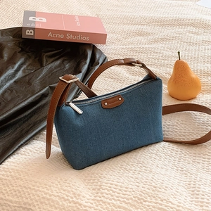 Retro denim shoulder bag with brown leather trim and silver zipper on a cozy fabric background