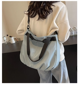 Detail of light blue pleated tote bag with black woven handles and adjustable shoulder strap