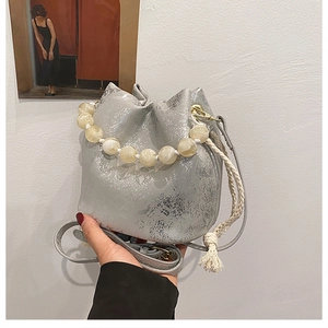 Detail of silver textured bucket bag with marble bead handle and woven shoulder strap