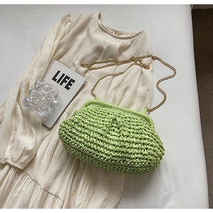 Detail view of woven straw shell bag in bright green with golden chain on white dress