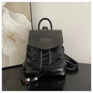Detail of black pleated drawstring backpack with metallic plate and decorative beads
