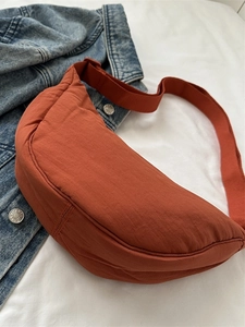 Caramel nylon crescent crossbody bag with wide shoulder strap on denim background