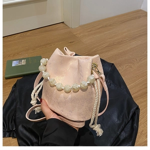 Close-up of metallic pleated bucket bag with large pearl handle and drawstring detail