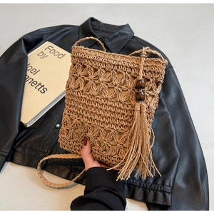 Detail of woven straw bucket bag with floral hollow patterns and tassel charm