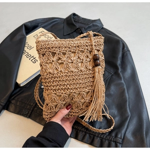 Detail of hand-woven straw bucket bag with diamond hollow pattern and tassel with wooden beads