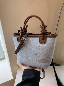 Denim bucket bag with floral embroidery, leather handles, and adjustable shoulder strap