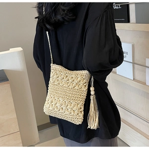Detail of woven straw bucket bag showing hollow floral crochet pattern and tassel with wood bead