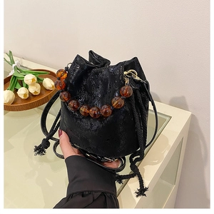 Detail of black drawstring bucket bag with cracked texture and amber beaded handle
