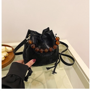 Detailed view of black textured bucket bag with amber beads and drawstring closure
