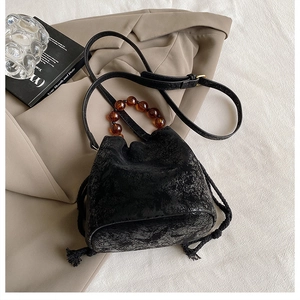 Detailed macro view of black pleated bucket bag with amber beaded handle and drawstring cord