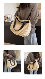 Detail of a large cream canvas tote bag with black straps worn by a model in a cozy room