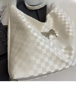 Close-up of white checkerboard tote bag featuring a decorative silver metal butterfly