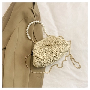Detail of woven straw cloud bag with large pearl handle and gold chain on neutral fabric