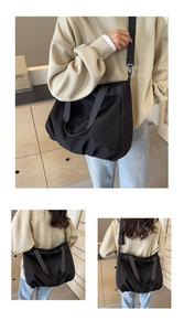 Detail of black nylon tote bag showing adjustable wide strap and pleated fabric texture