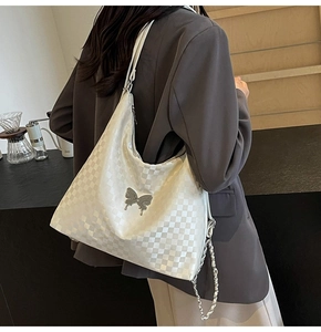 Detail of white checkered hobo bag featuring silver butterfly charm and chain strap
