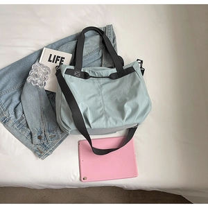Close-up of light blue canvas tote bag featuring wide black handles and detachable shoulder strap
